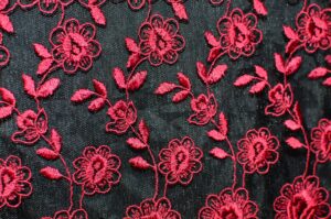 Seamless background of creative flowers with leaves embroidered on black fabric with red thread creating symmetrical pattern on thick textile
